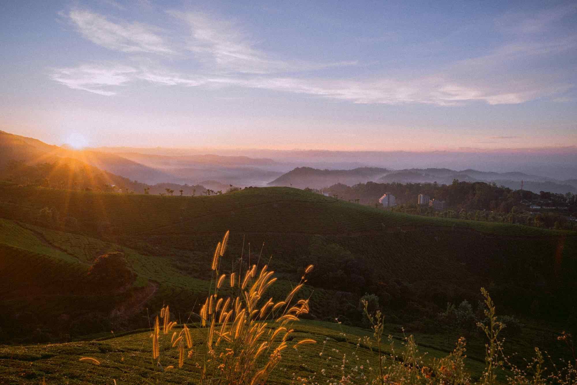 Sunrise over green terraced hills with a clear sky and some scattered clouds.