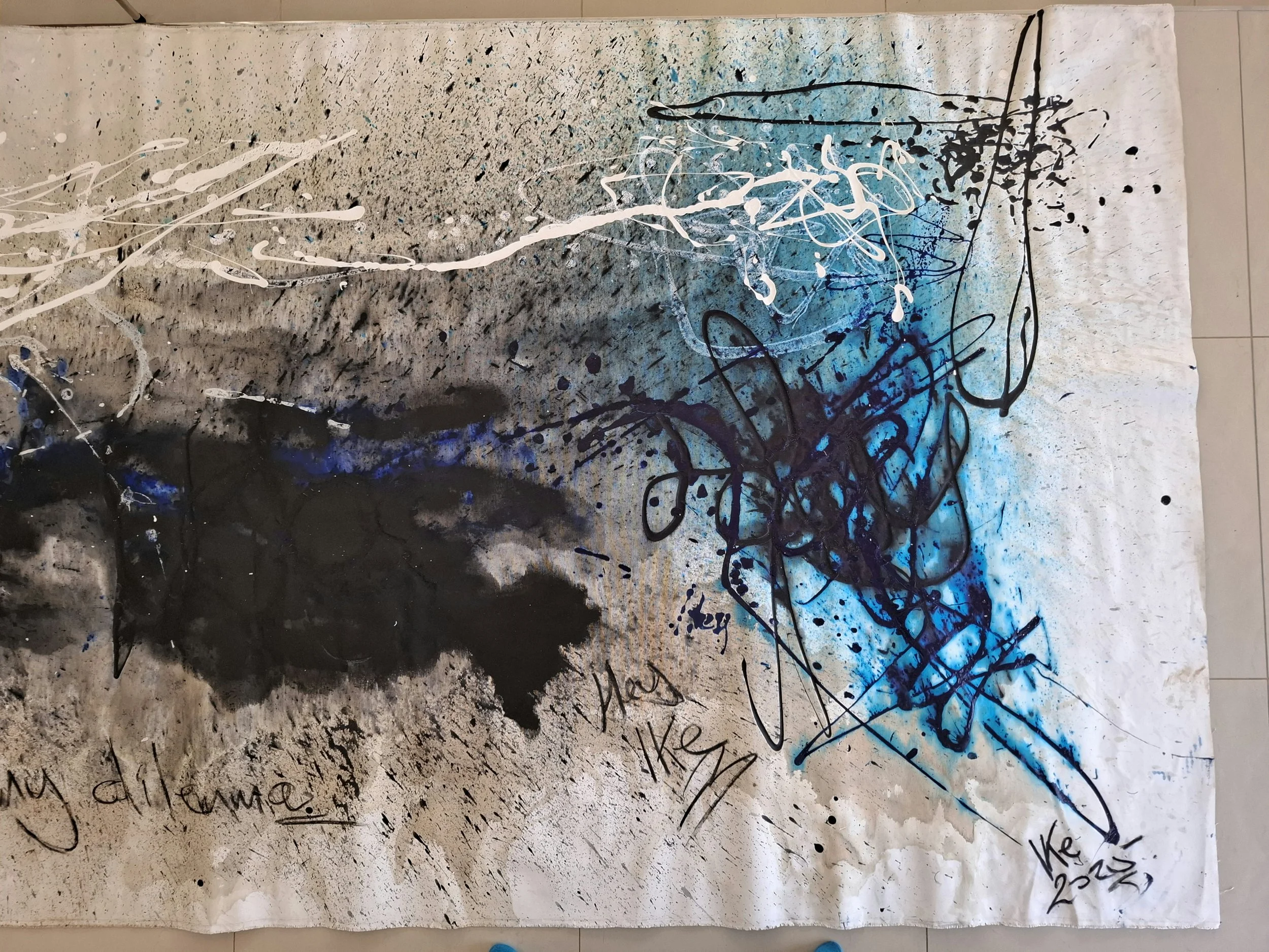 Abstract painting with black, white, and blue splashes, lines, and scribbles on paper.