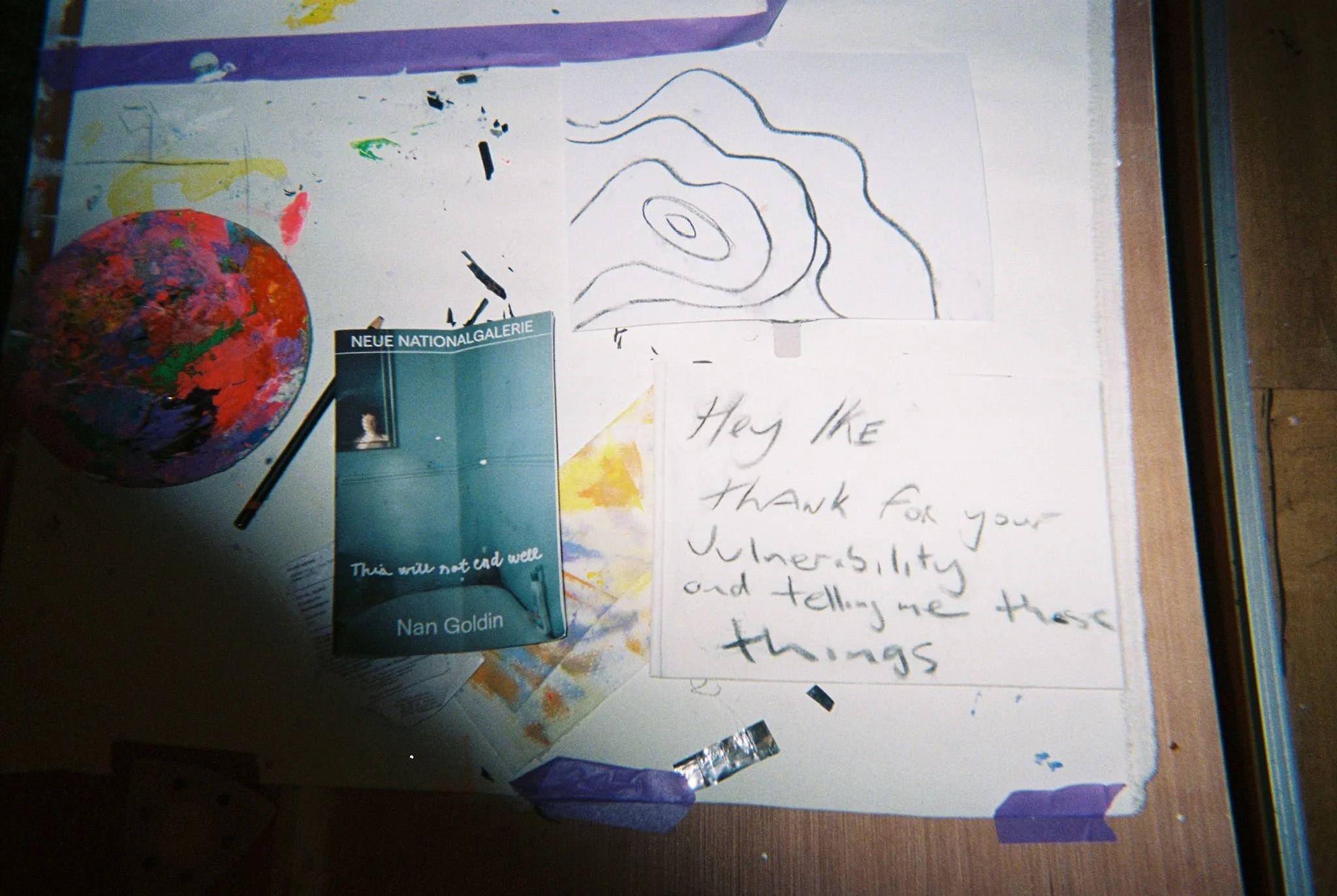 An art desk with a painted globe, a small print of an art gallery, a handwritten note, a line drawing, and various art supplies.