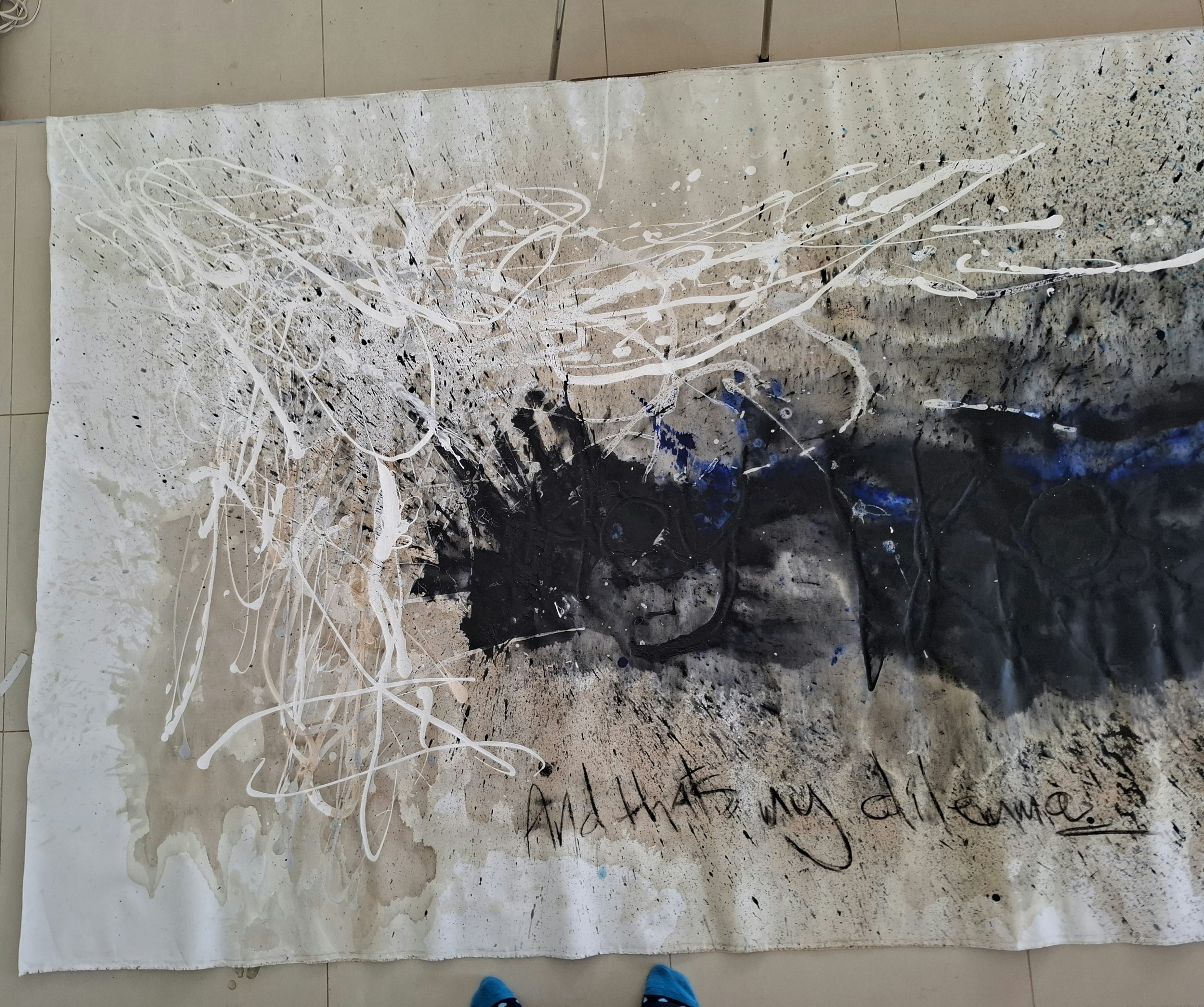Abstract mixed media artwork featuring splatters, drips, and scribbles in black, white, and blue on a large sheet of paper.
