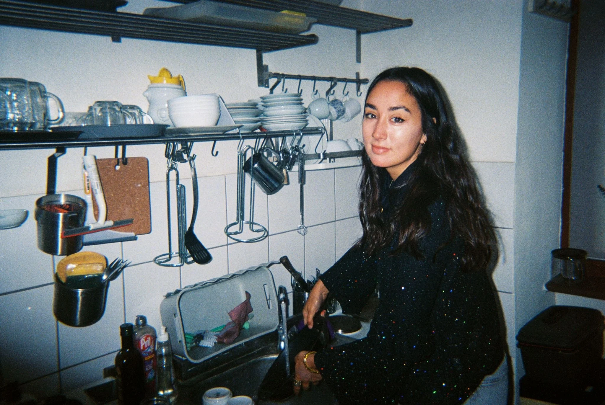 A young woman with long dark hair standing in a kitchen, washing dishes at the sink.