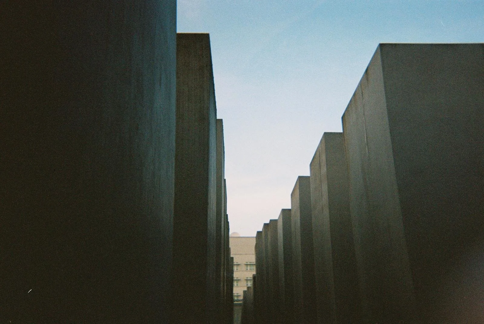Row of large, dark concrete blocks or structures, with some buildings visible in the background and a clear sky overhead.