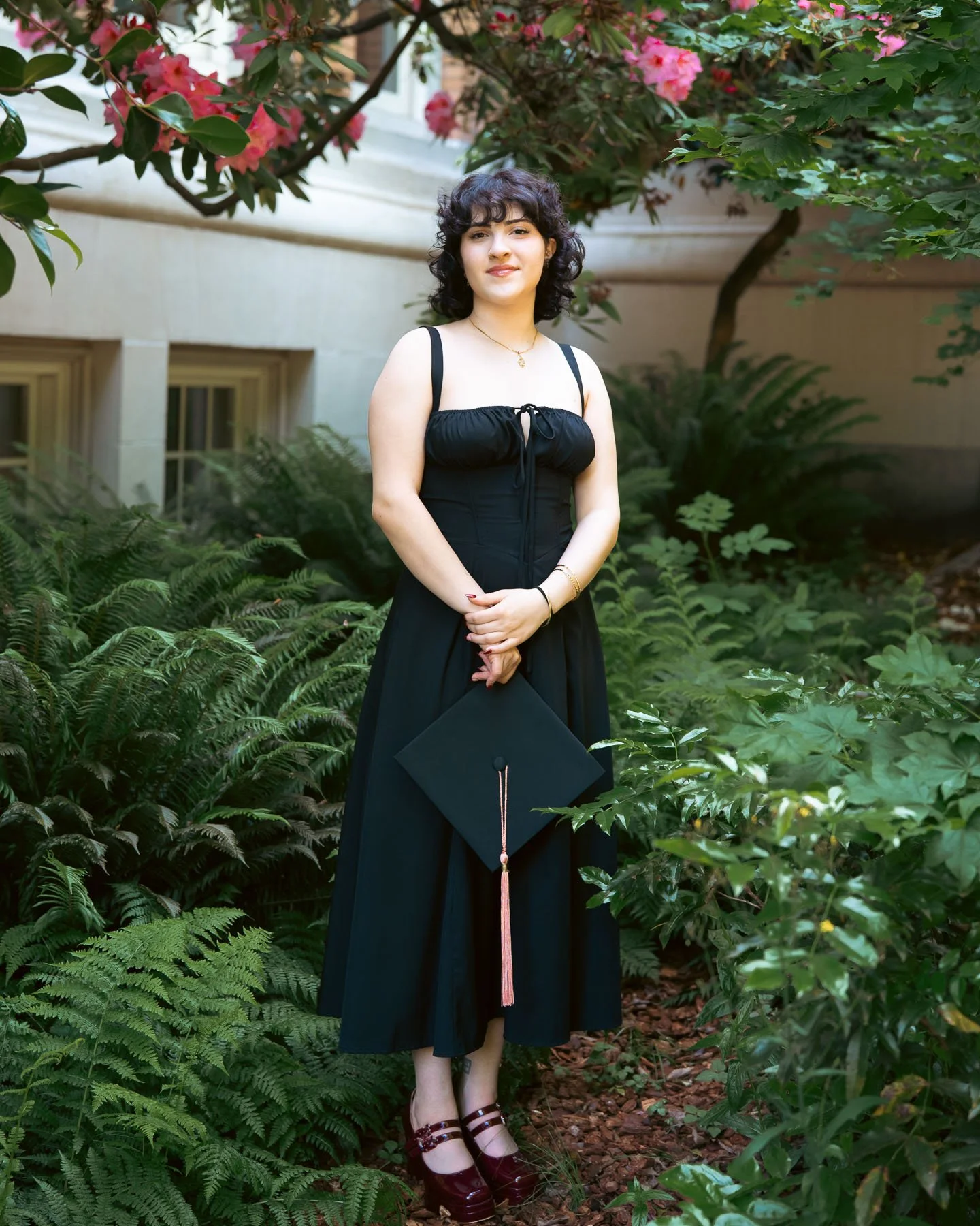 A university of Portland graduate surrounded by ferns and flowers posing for her graduation photos