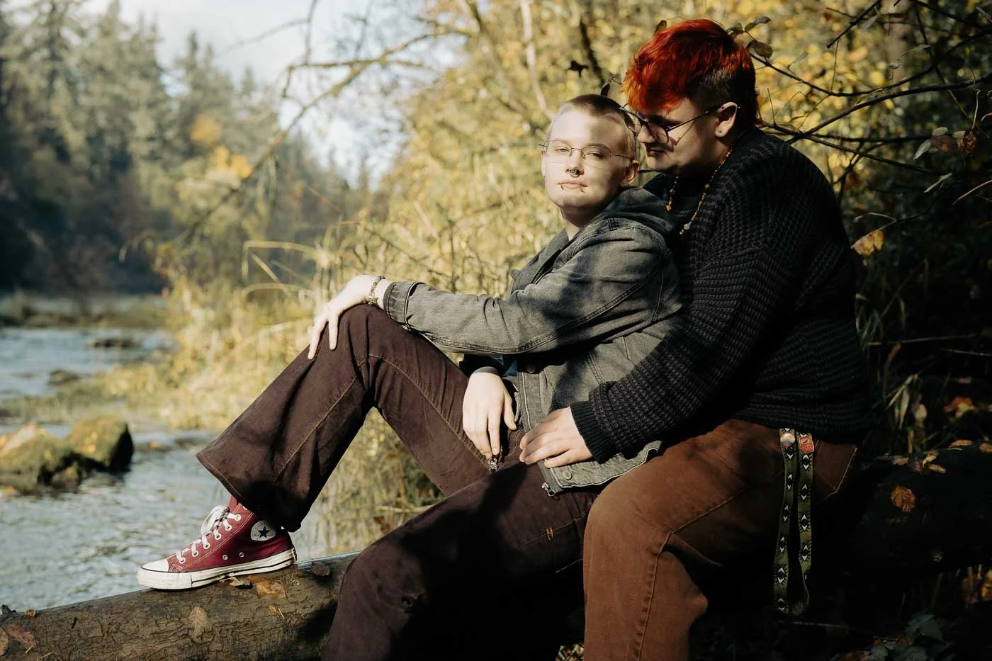 A high school couple sitting on a downed tree next to a river with fall colors