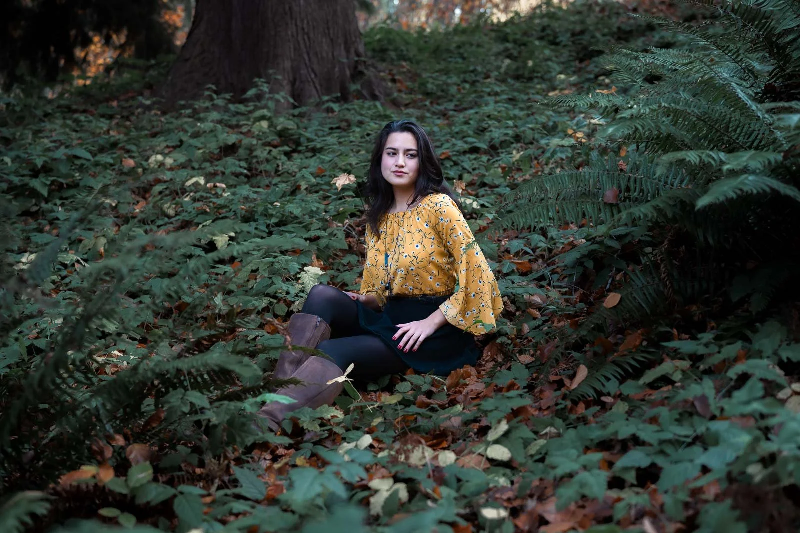 A high school girl in yellow sits on the ivy covered ground in Hoyt Arboretum