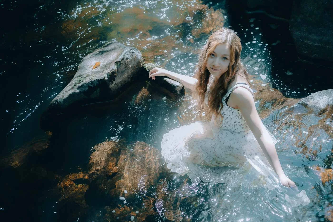 A girl in a white dress wades through a river