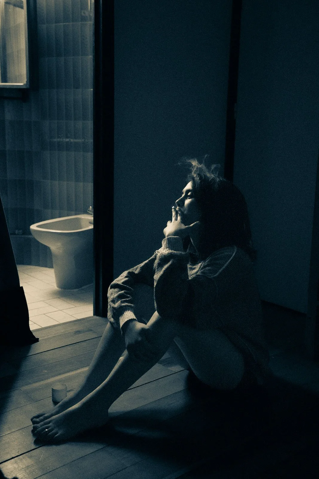 A girl sits in a blue lit room smoking a cigarette