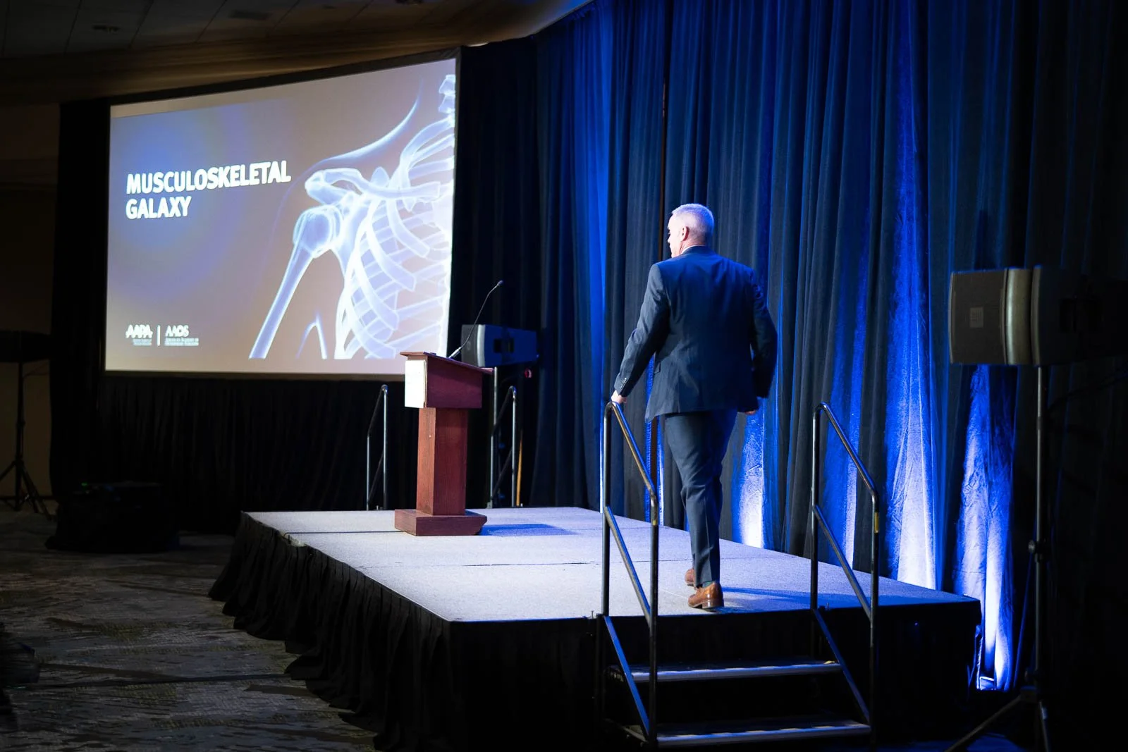 A man walks onto stage for a presentation during the 2025 APHL annual meeting