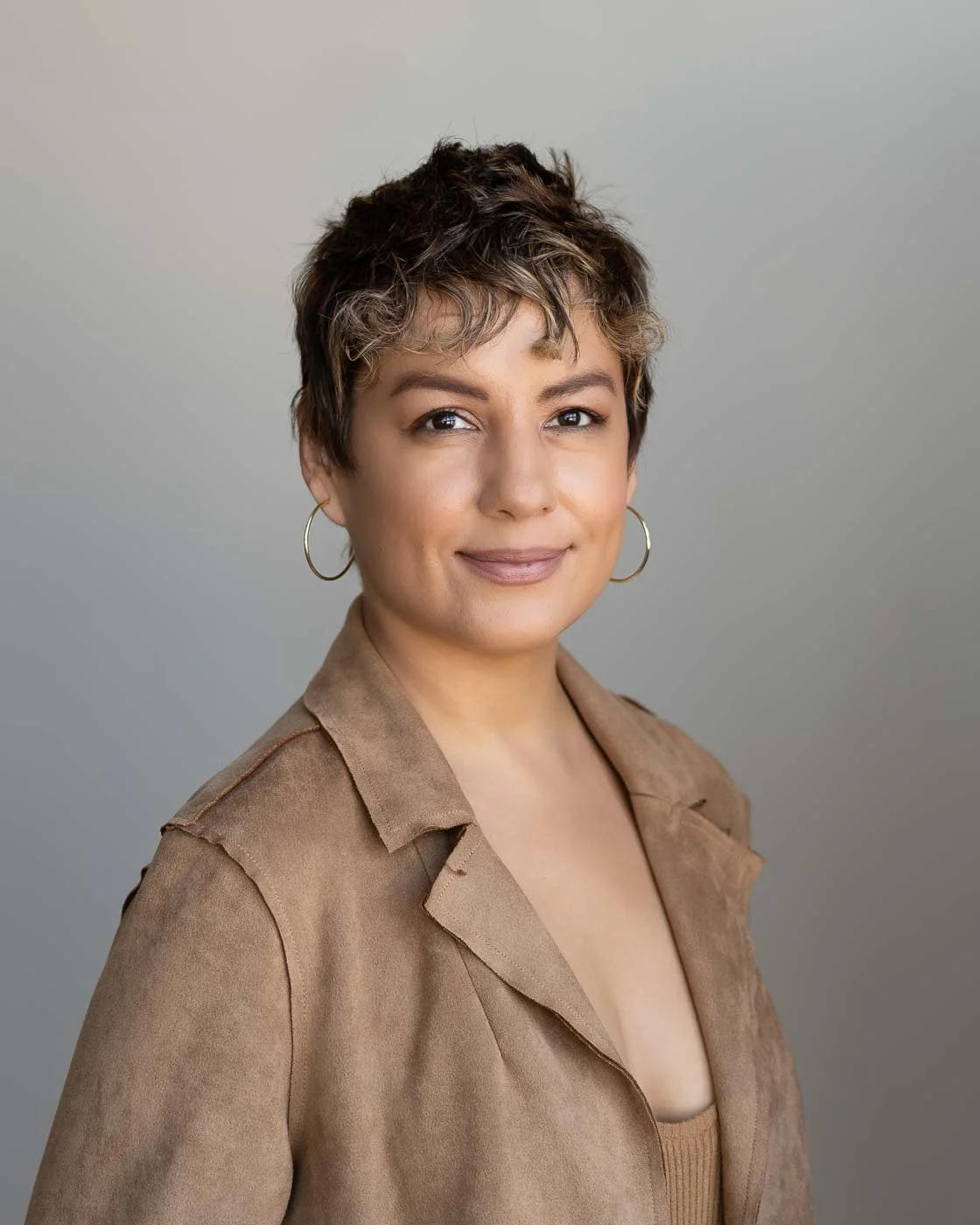  Young professional woman in a brown jacket and short wavy hair posing for a headshot 