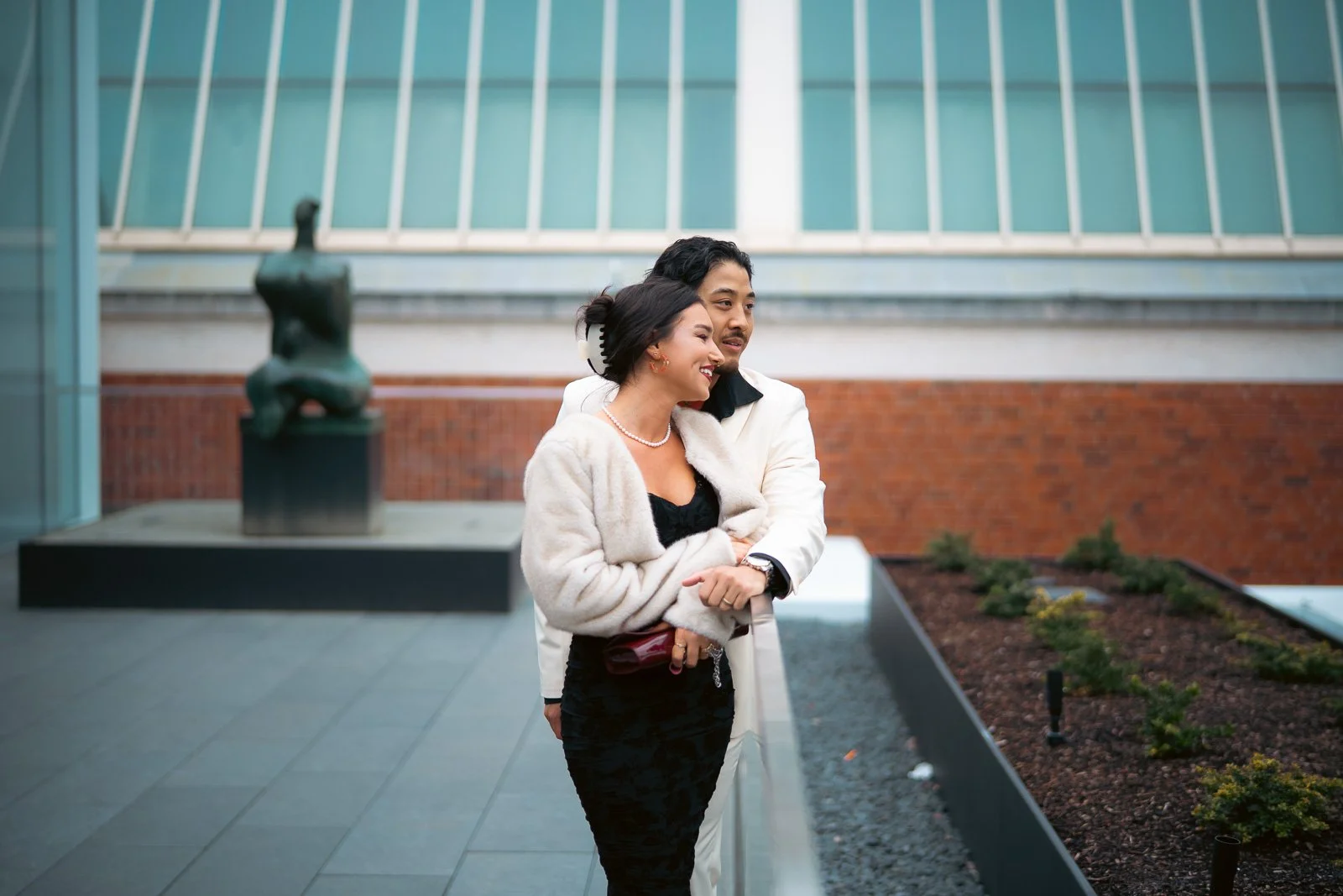  A smiling chic couple standing on a balcony with a statue behind them 