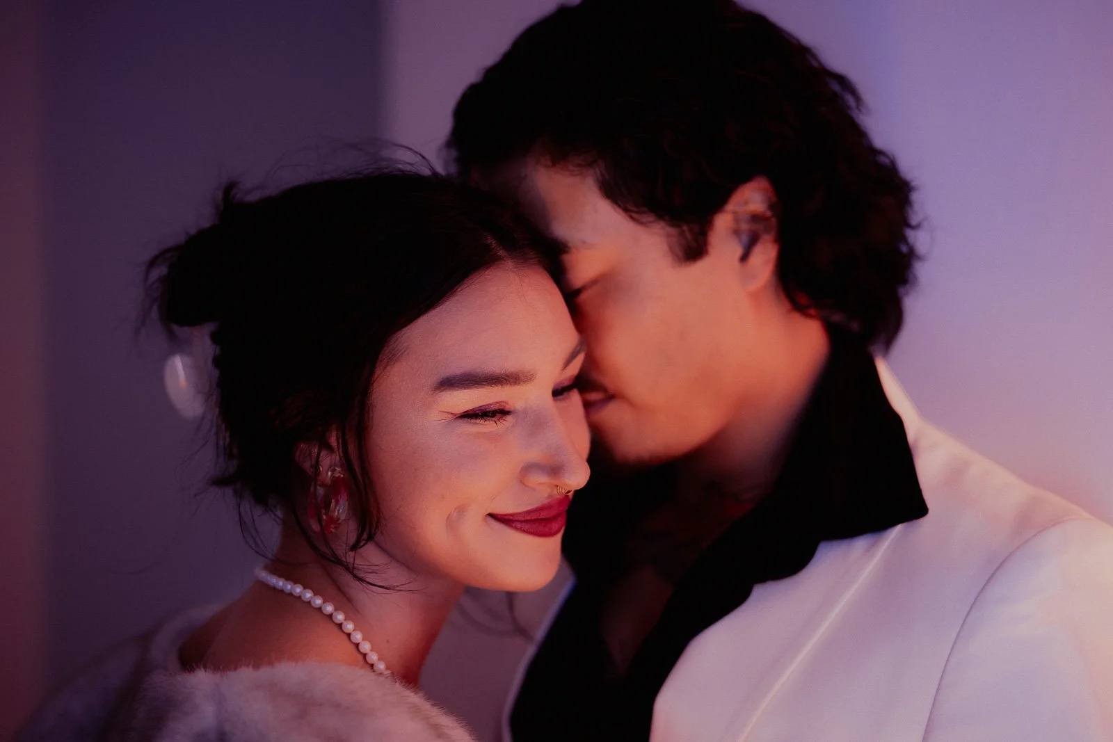  A dressed up couple leaning their faces together, lit by neon lights 
