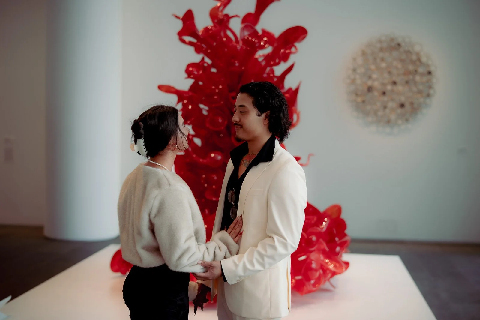  An elegant couple poses for engagement photos in front of a large red glass sculpture 
