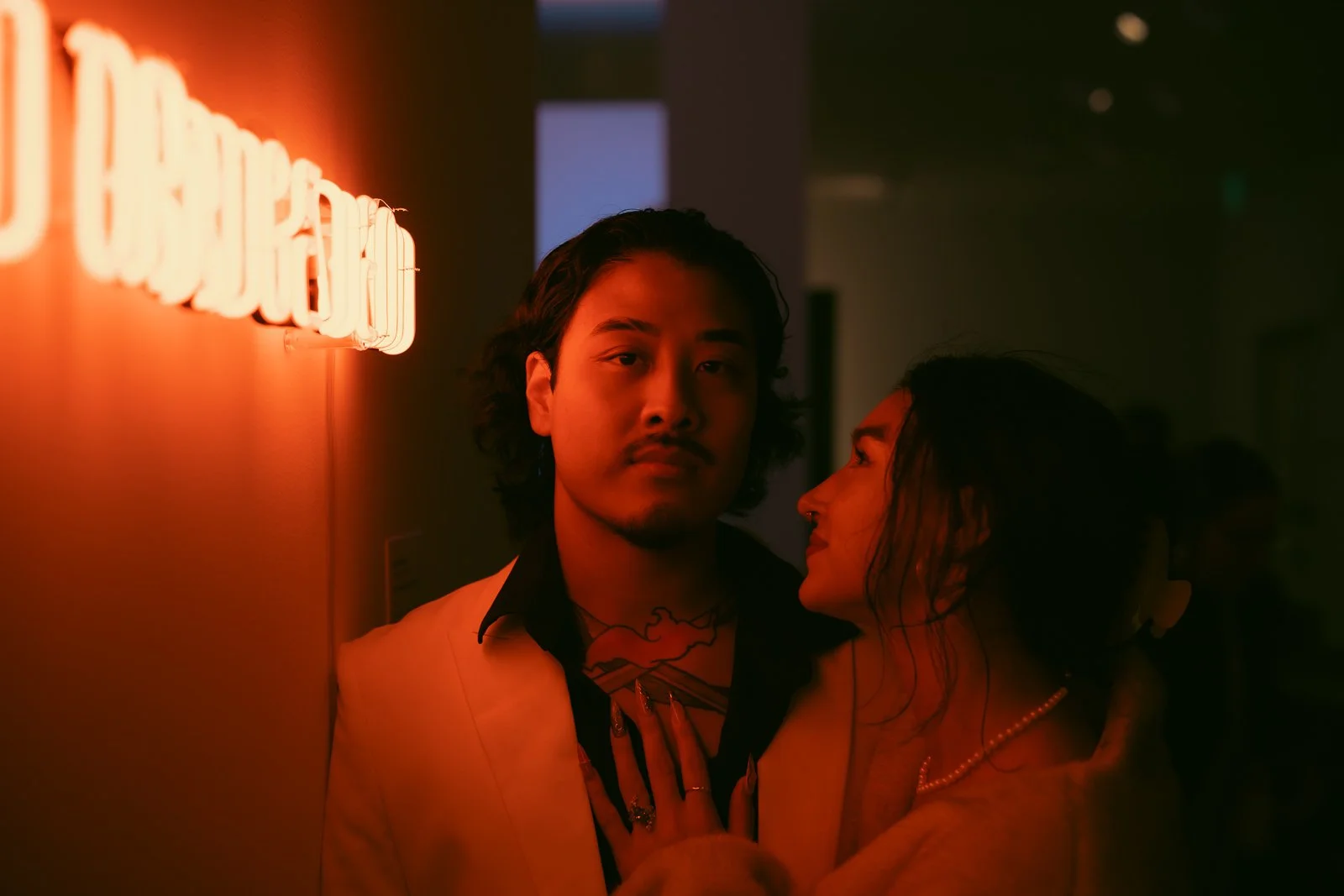  A moody portrait of a couple lit by the red lights of a neon sign at a Portland Art Museum exhibit 