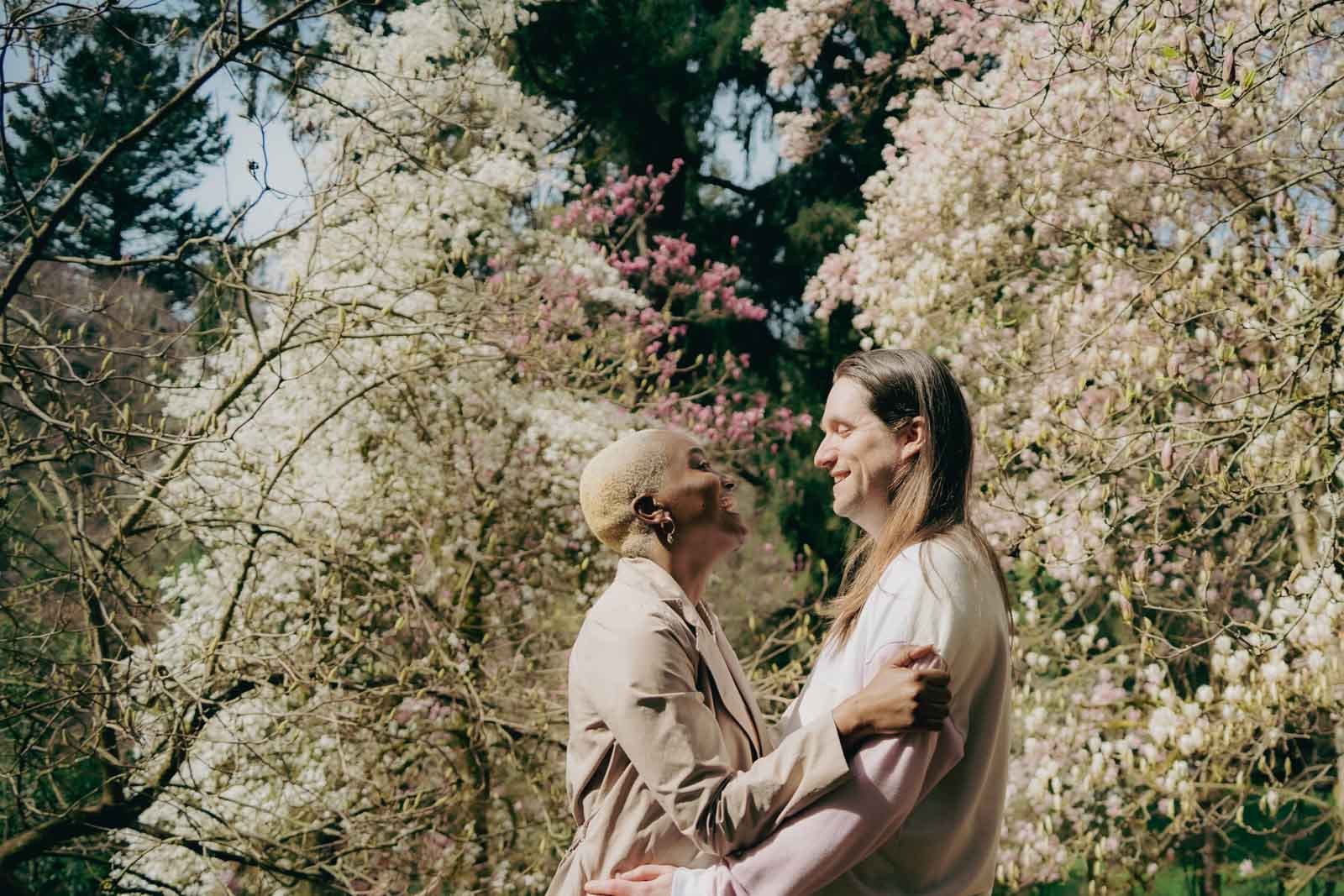  A couple holding each other and laughing in front of large flowering trees 
