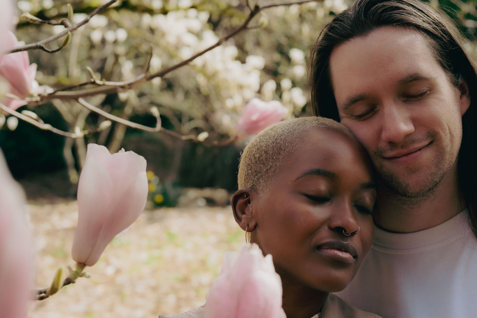  A couple tenderly lean into each other and close their eyes in a grove of flowering trees 