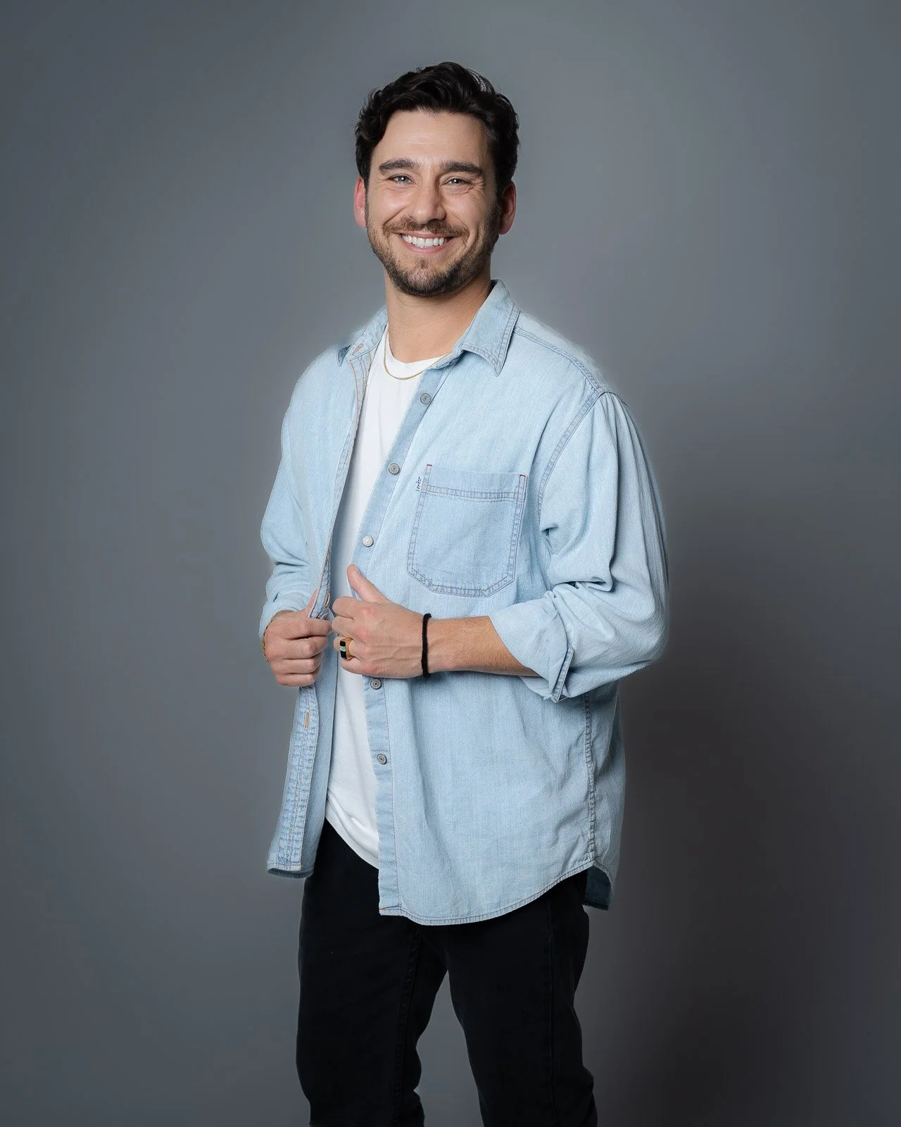 A man smiles and looks at the camera, wearing a blue button up shirt