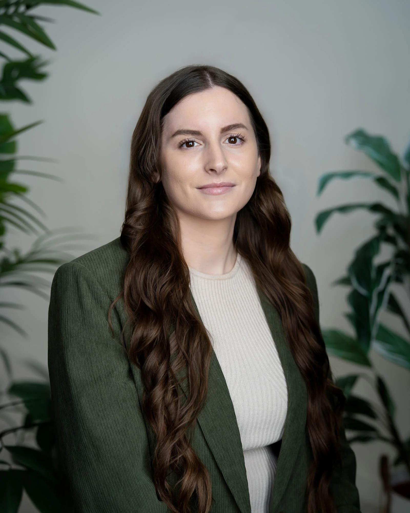 A woman with long wavy brown hair wearing a green blazer and white blouse with a warm and inviting expression