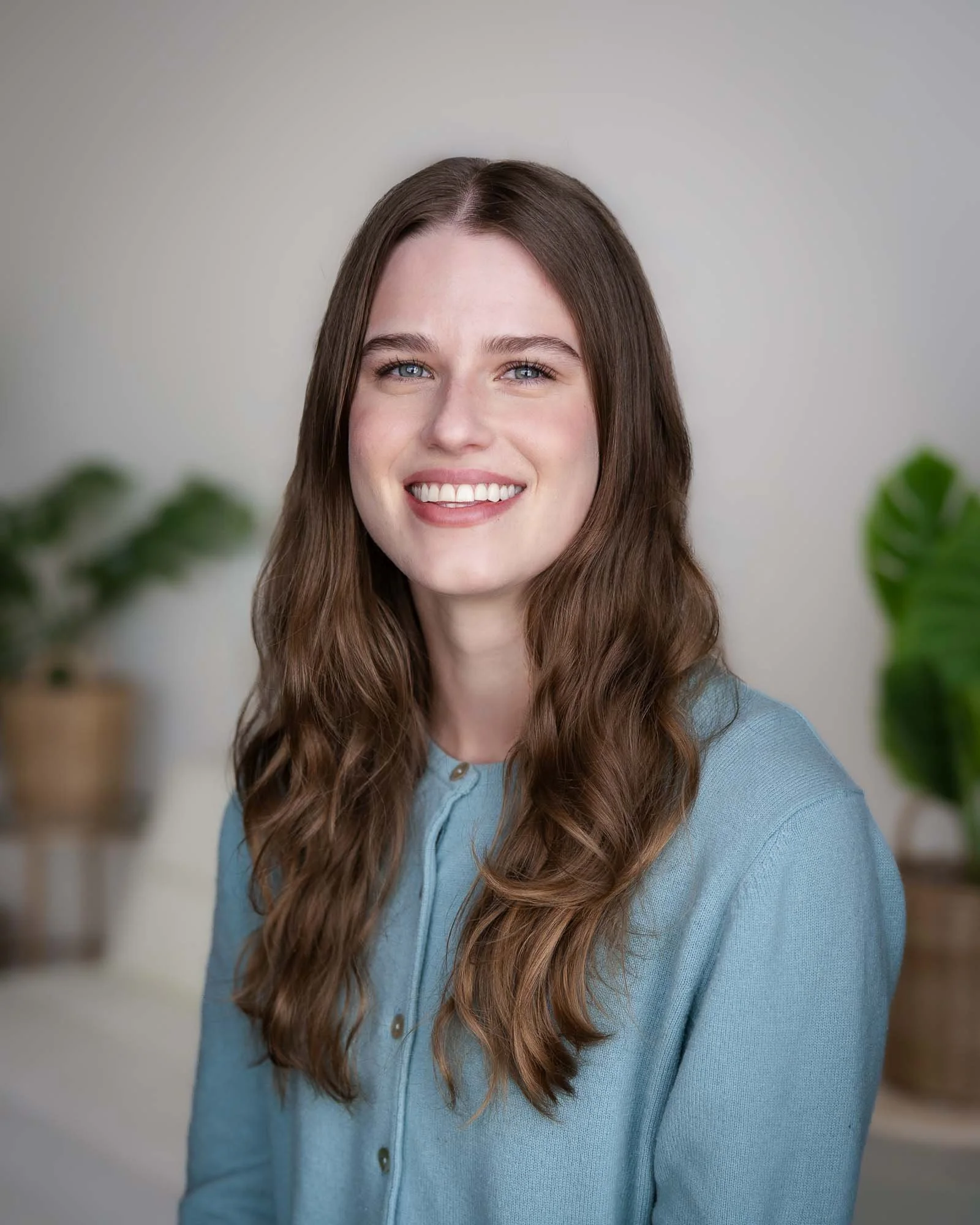 A therapist at the Portland natural light studio, PDX-Portraits, smiling in a well lit room with plants in the background