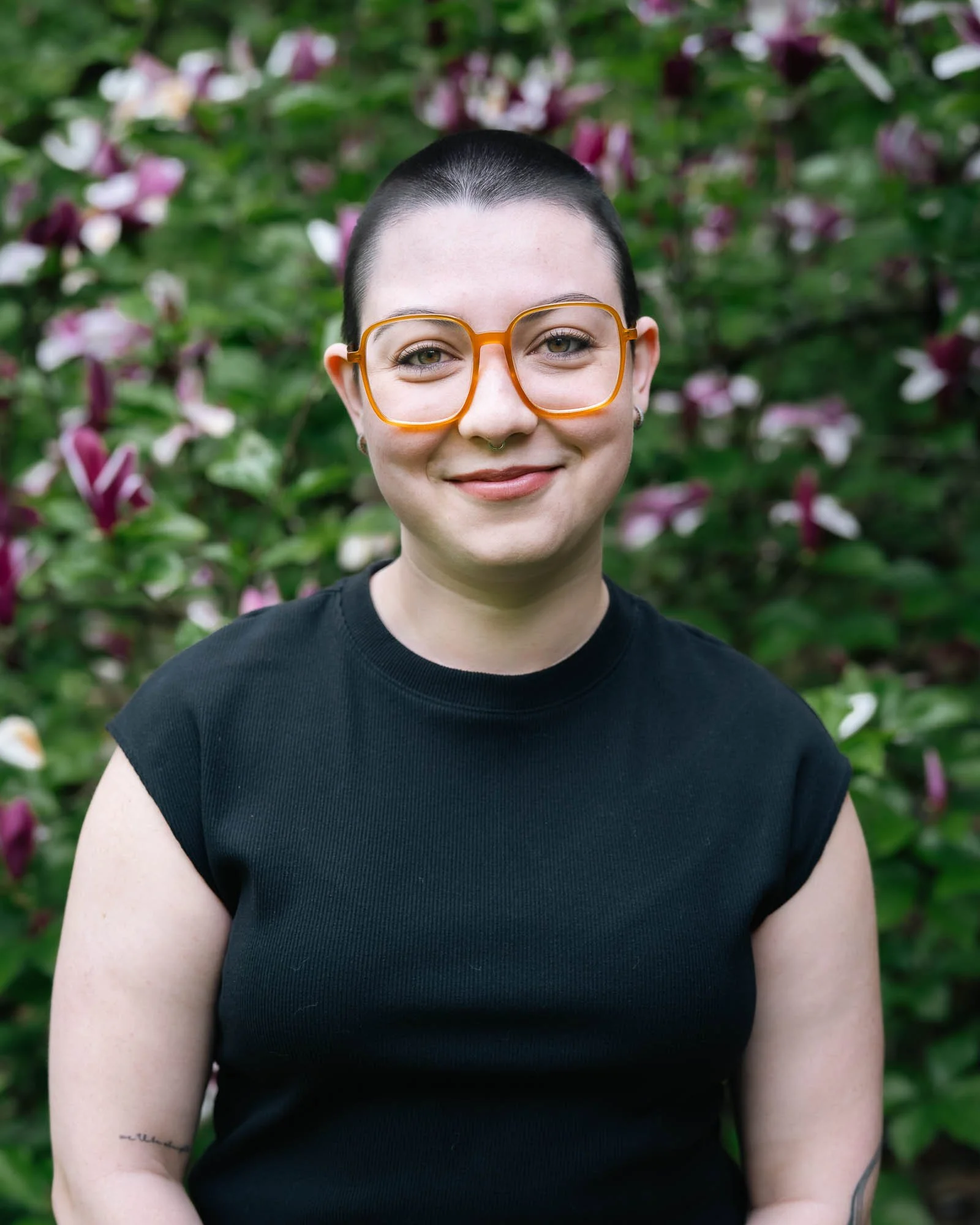 A young woman with short hair posing for her therapists headshot in the flowering gardens of Hoyt Arboretum