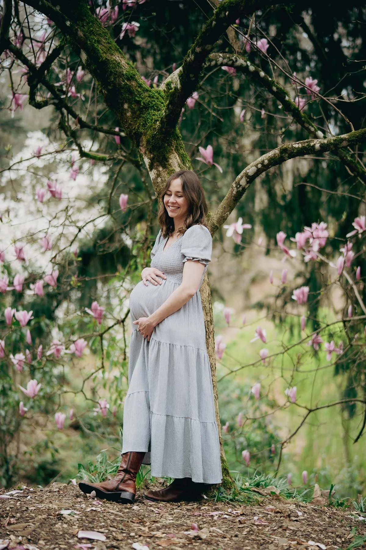 Pregnant woman in a flowing dress, smiling while leaning against a blossoming Magnolia tree