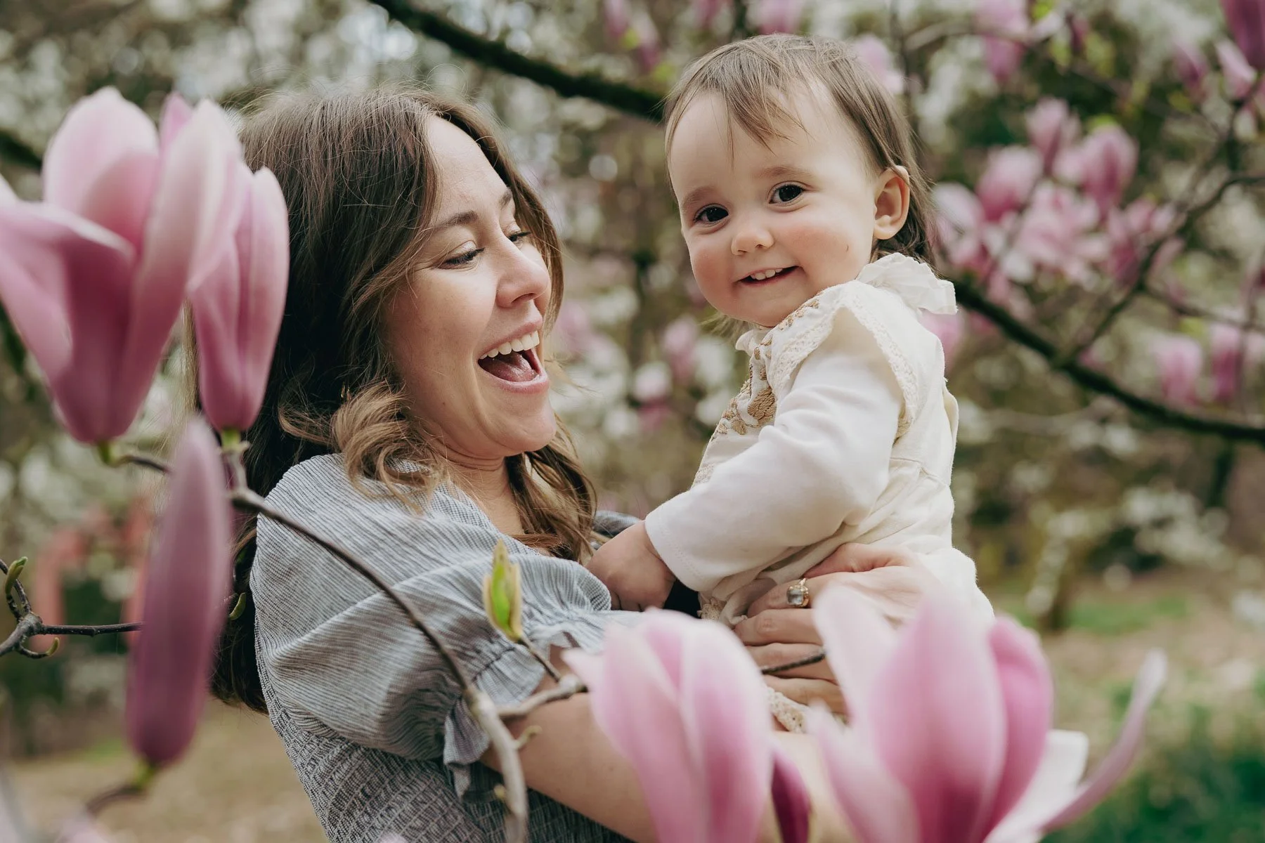 A pregnant mother and her child smile and laugh in a grove of flowering trees