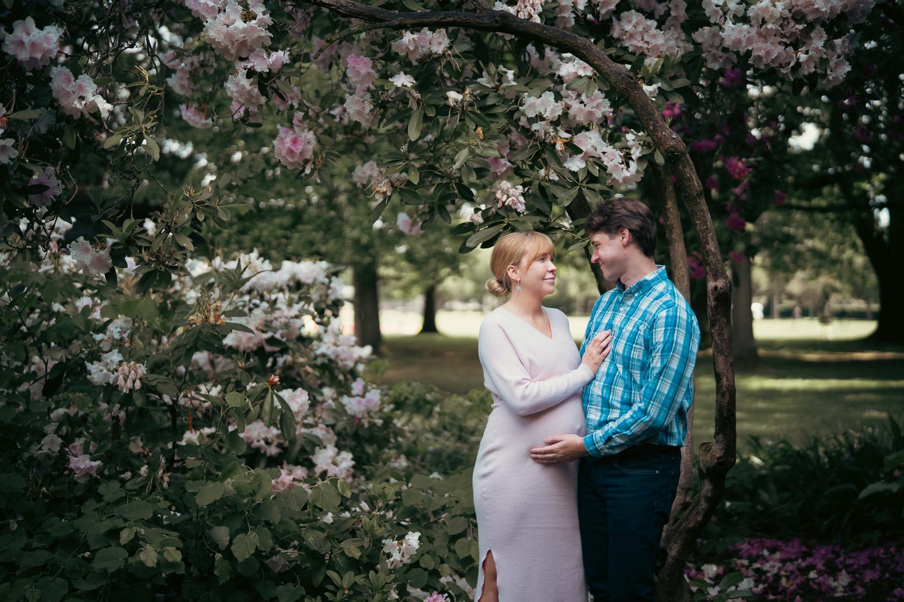 A smiling couple surrounded by flowering trees celebrating their pregnancy