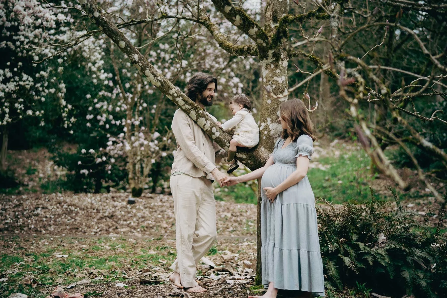 A pregnant woman holds her stomach while playing with her child and husband in a nature park