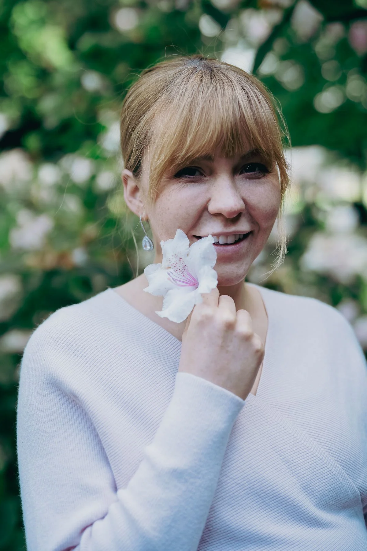 A smiling pregnant woman holds a flower to her face
