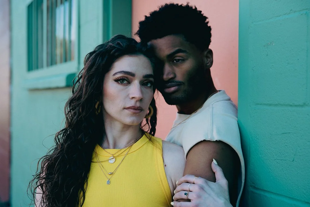 Fashion couple leaning together in front of a colorful wall