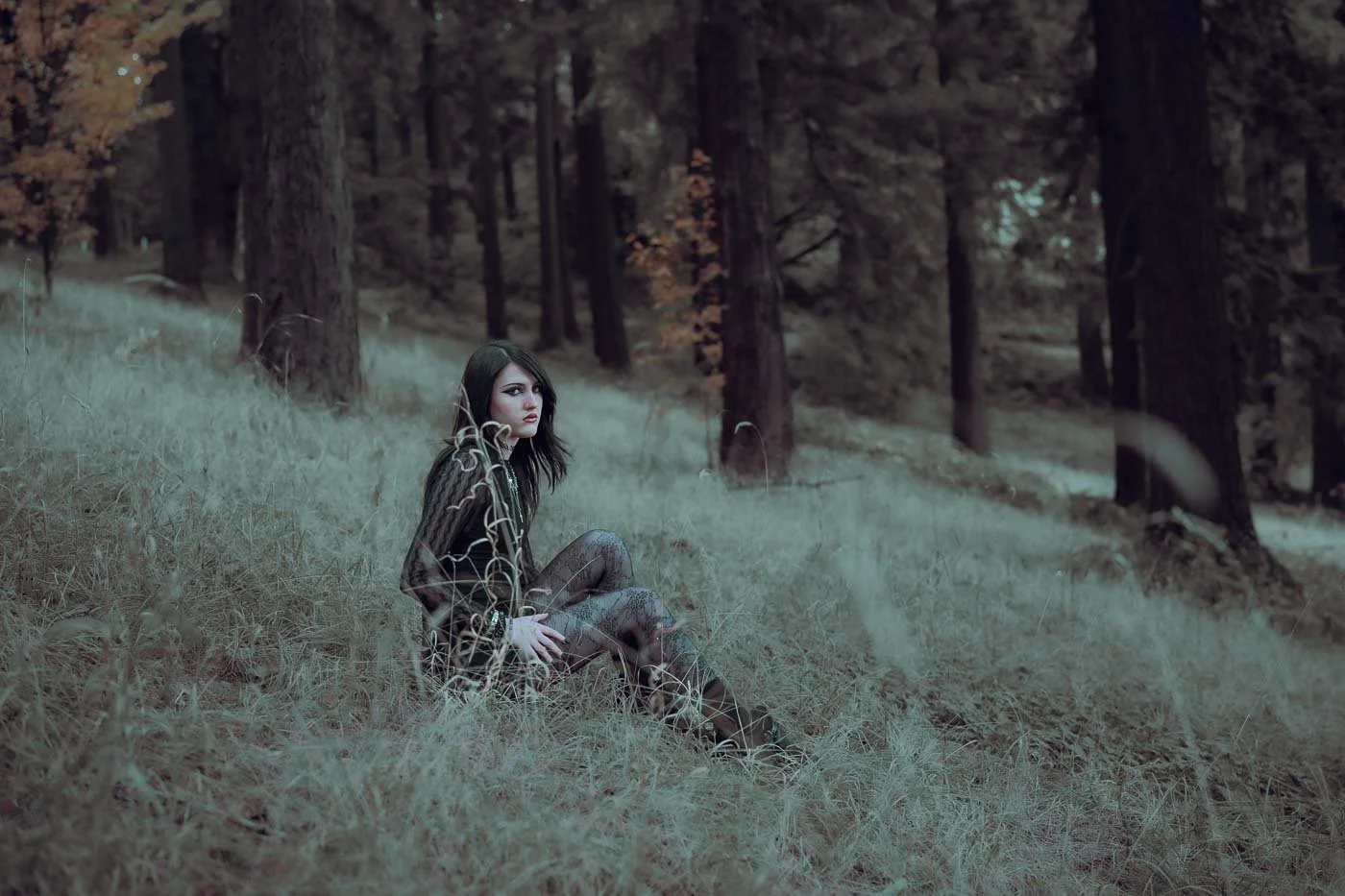Girl in emo clothing sitting amongst tall grass in a forest