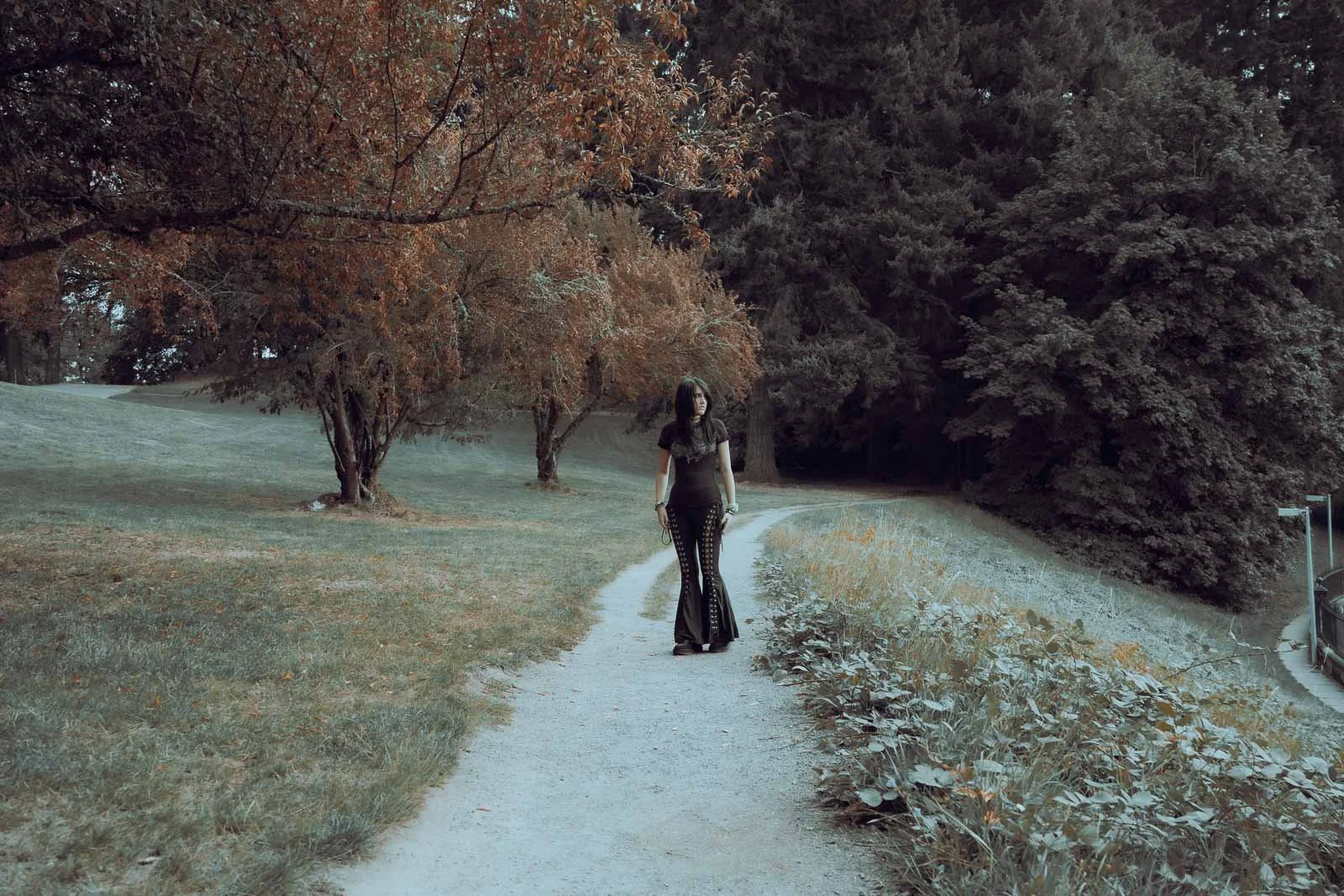 A girl in all black standing on a path surrounded by large trees