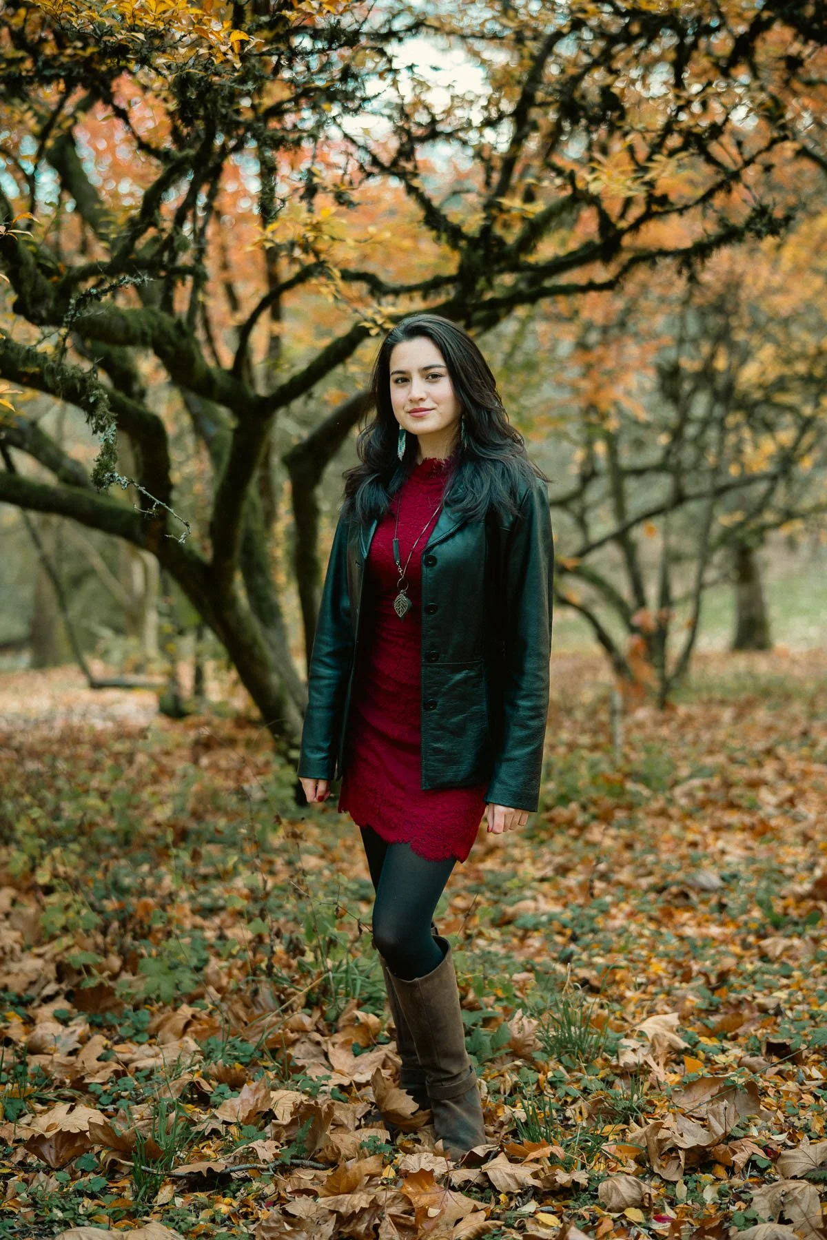 Full body senior portrait of a girl in a red dress and black leather jacket, surrounded by fall colors