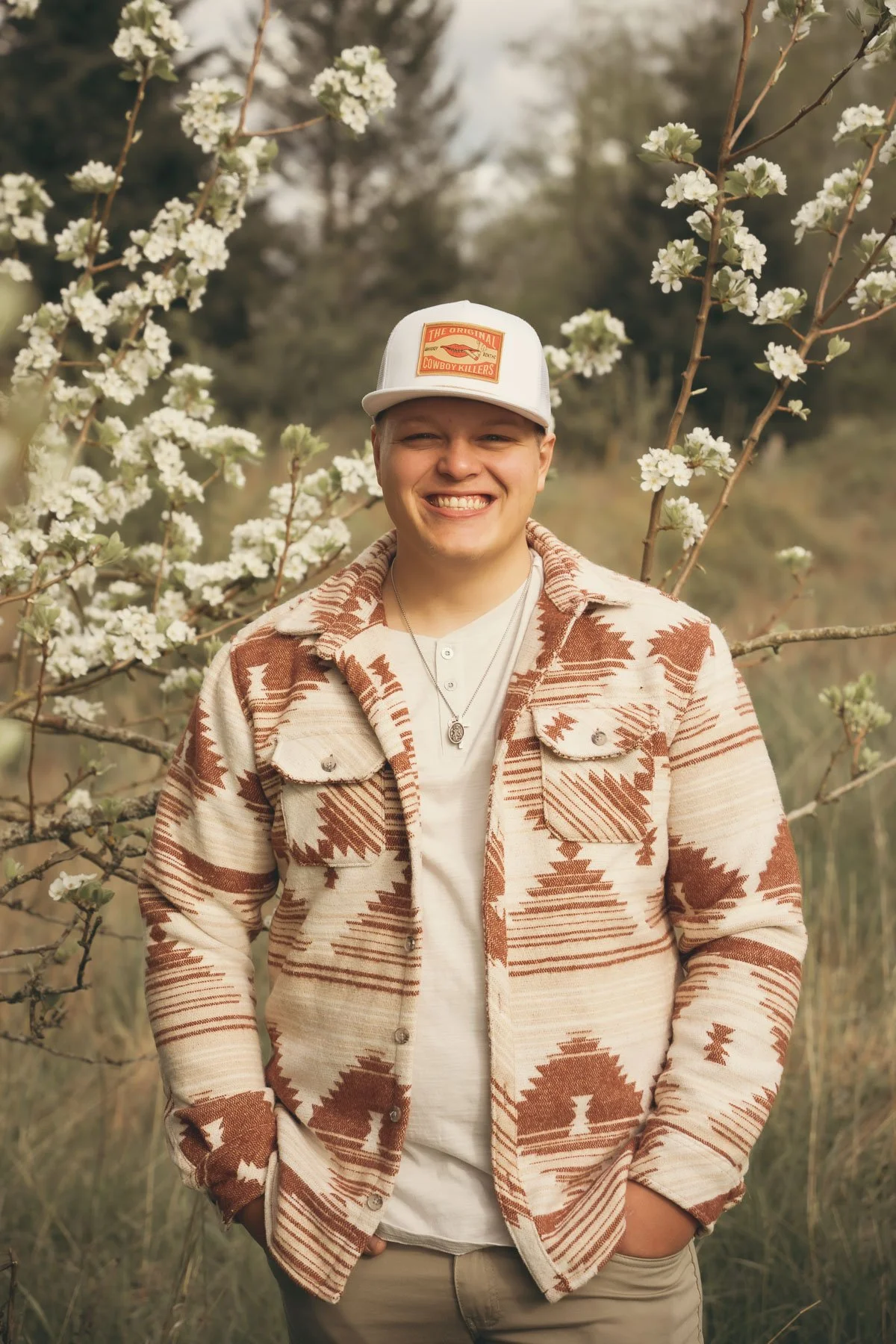 A grinning boy standing next to a flowering tree at Powell Butte for his senior portrait