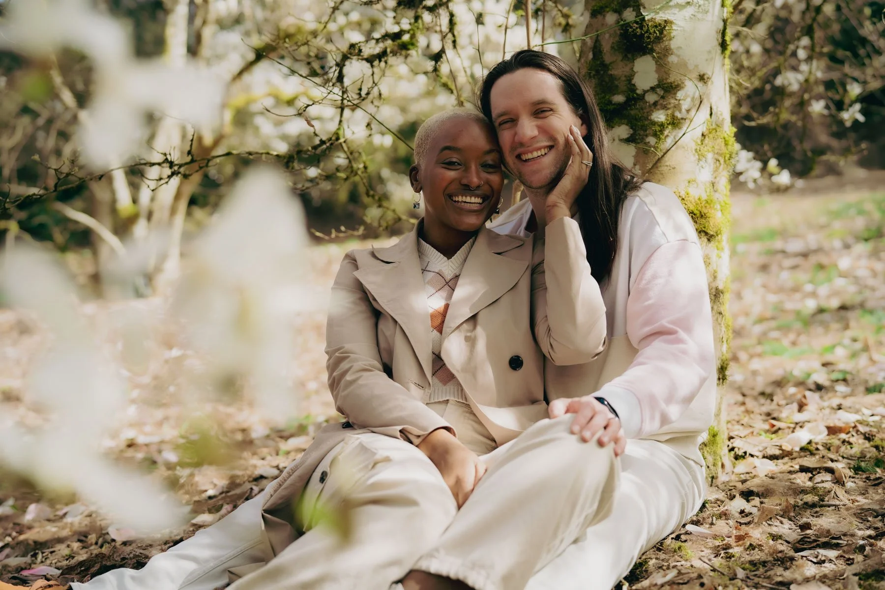 A smiling engaged couple sitting underneath a flowering Magnolia tree in Hoyt Arboretum
