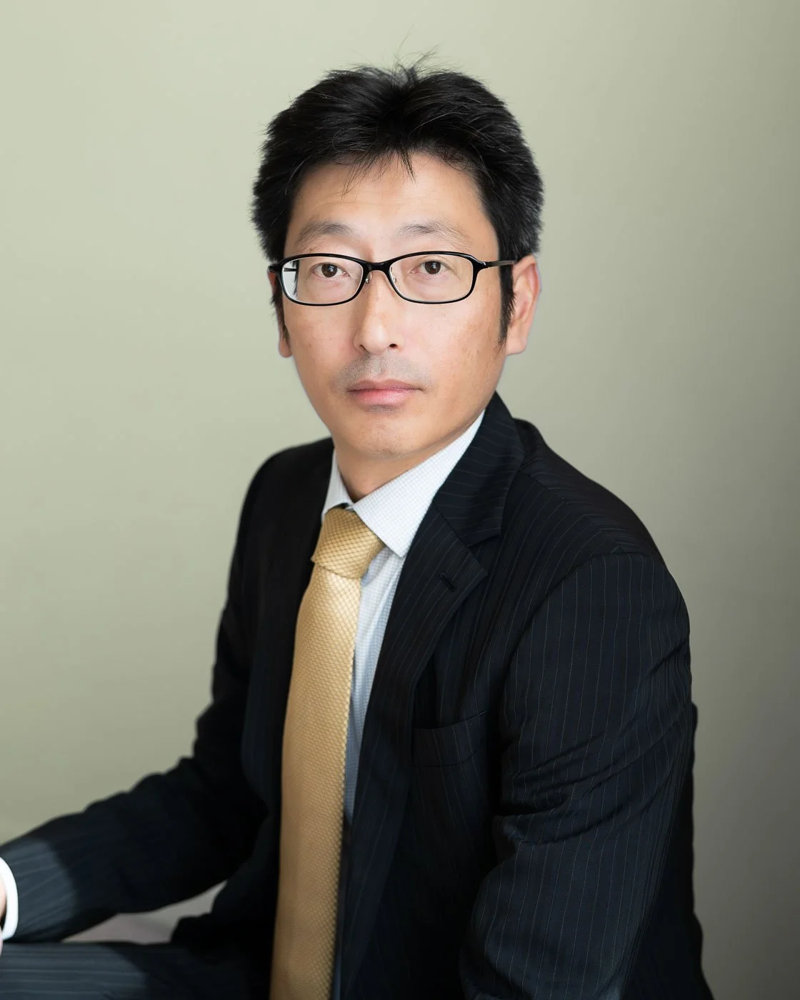 Headshot of a corporate employee, wearing a black blazer and gold tie