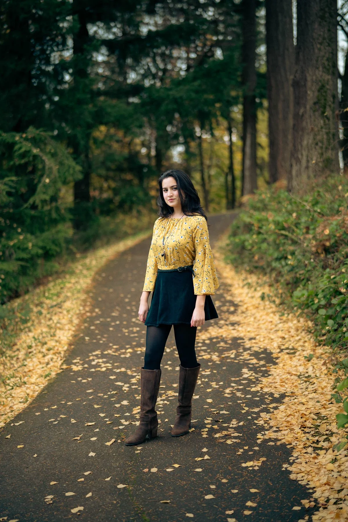 A girl posing for her senior photos surrounded by yellow leaves in the forest