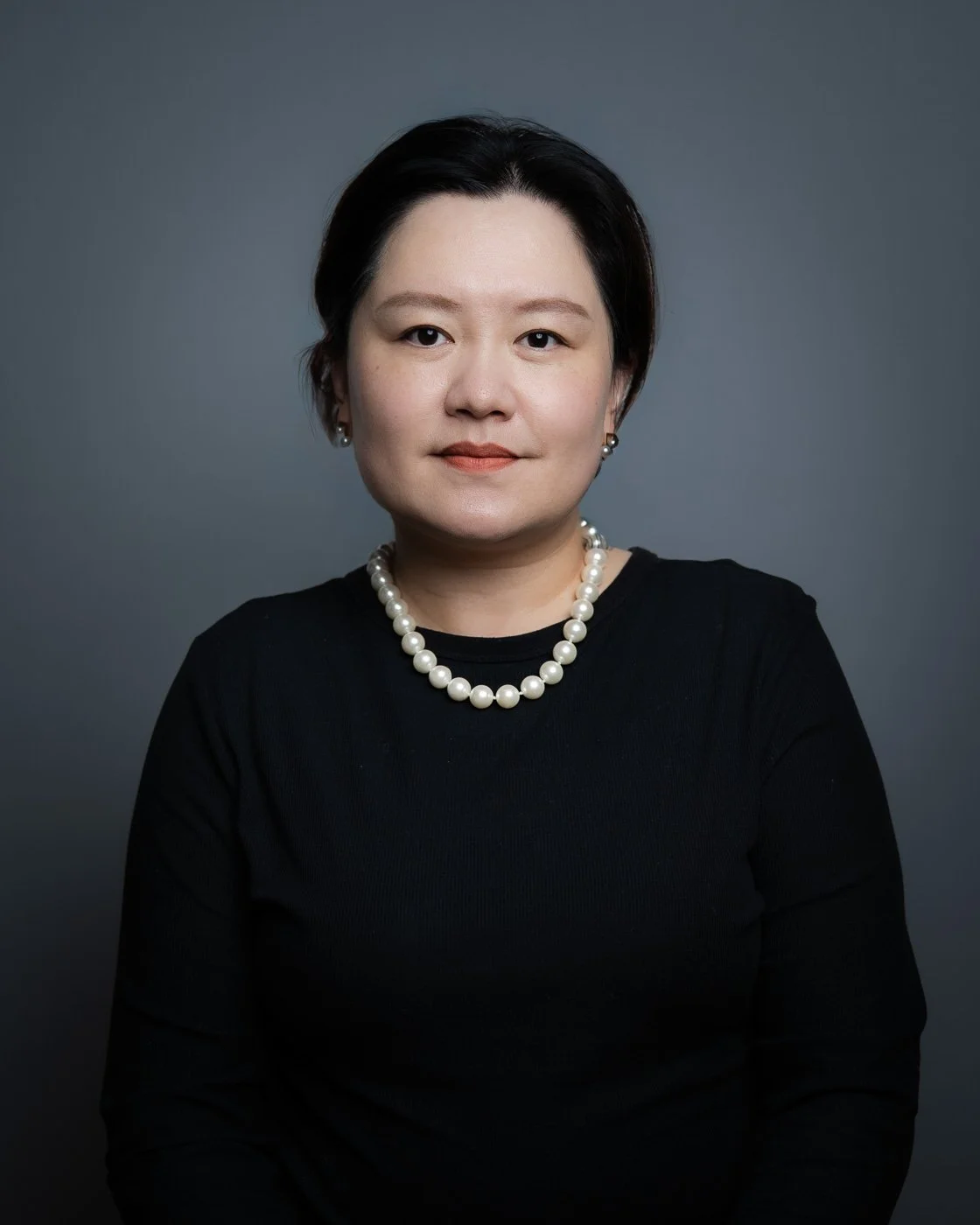 Headshot of a woman in a pearl necklace and black shirt