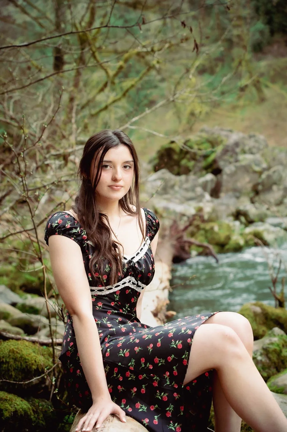 Girl in a dress with red flowers sitting on the edge of a river