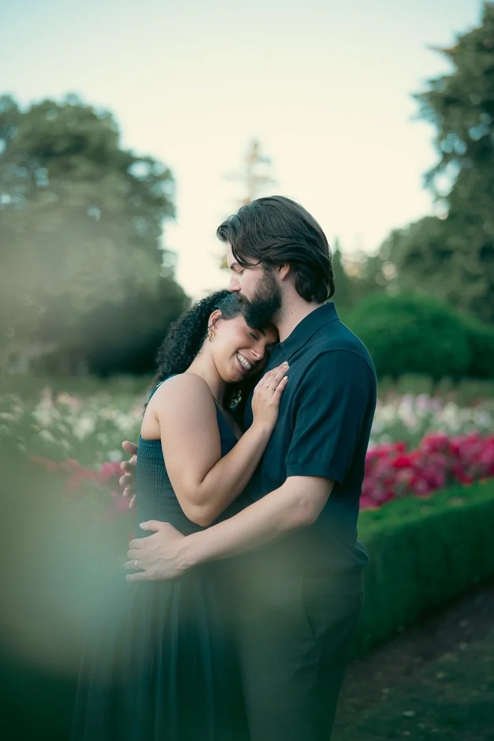 A couple smiles and holds each other with their eyes closed while surrounded by colorful roses