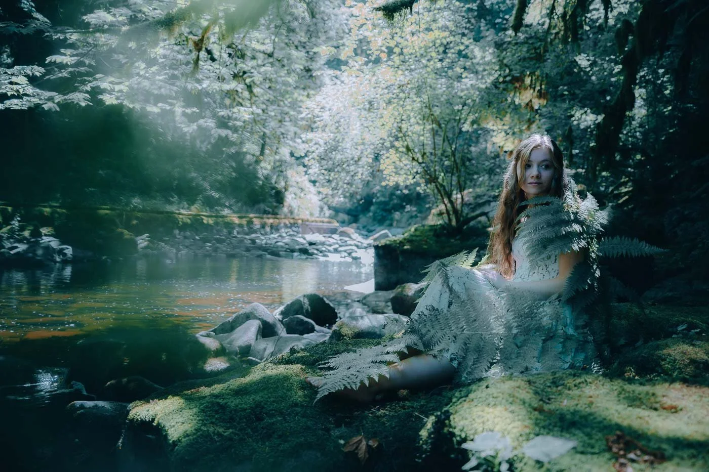 A young girl covered in ferns sitting next to a river