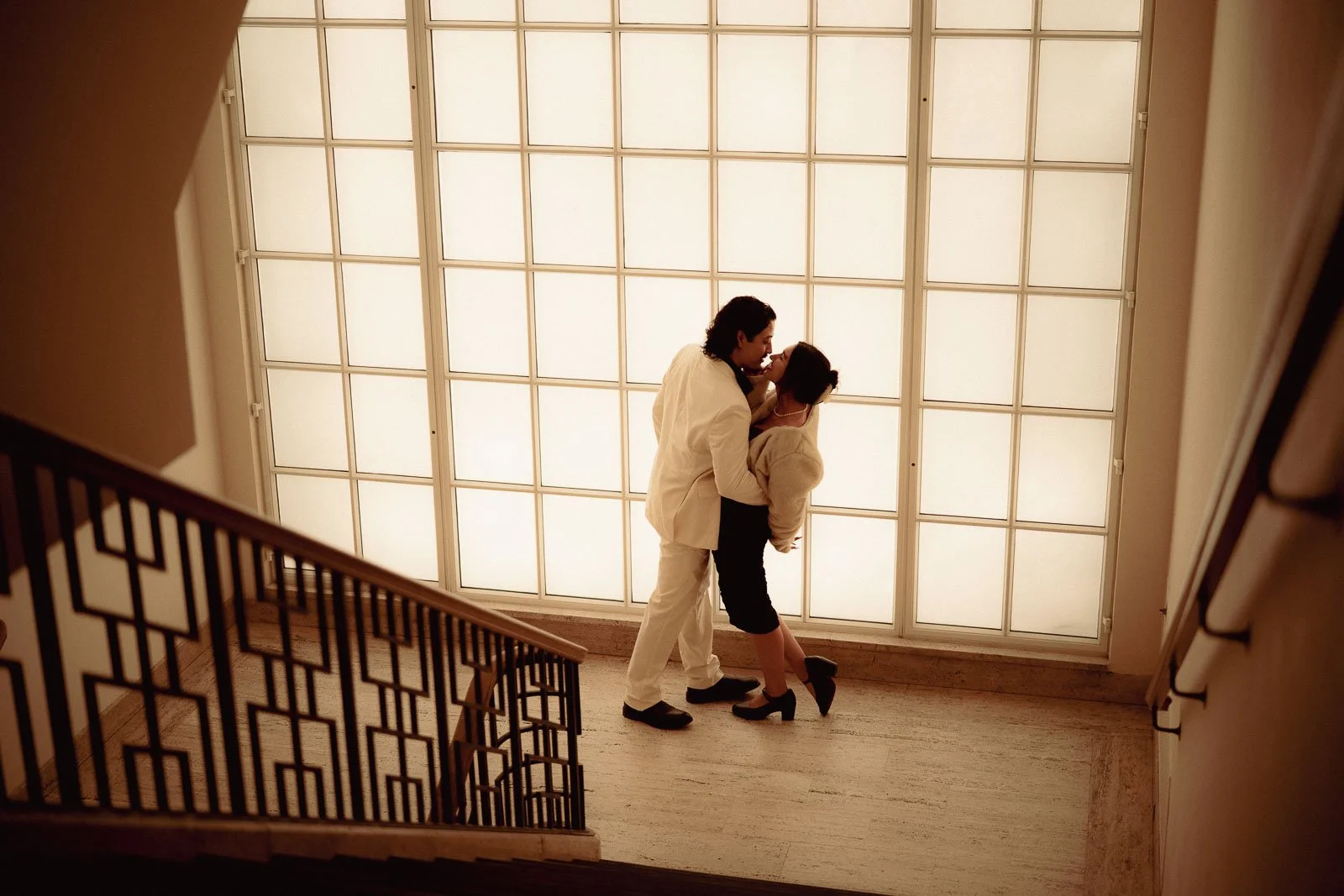 A couple dance in front of a large checkered window in an art gallery