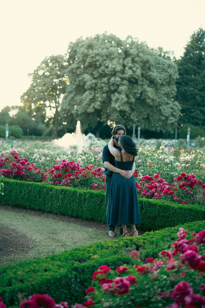 A couple swaying in a rose garden with a water fountain in the background