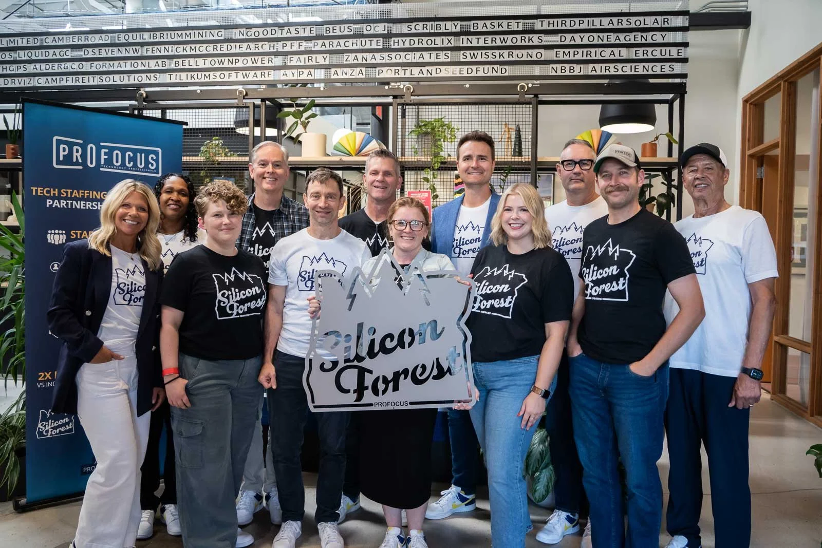 A group of people smiling with a Silicon Forest sign, at the Pro Focus event