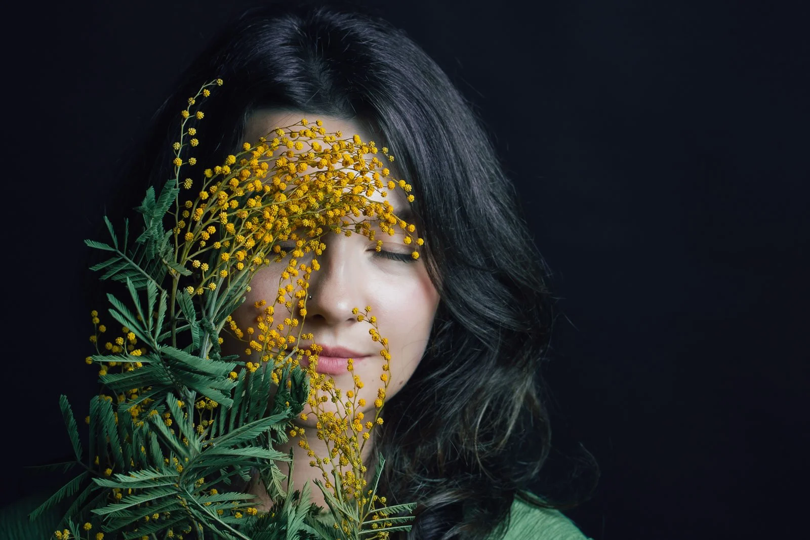 Female fashion model with her eyes closed, holding a small bouquet of yellow flowers obscuring half of her face