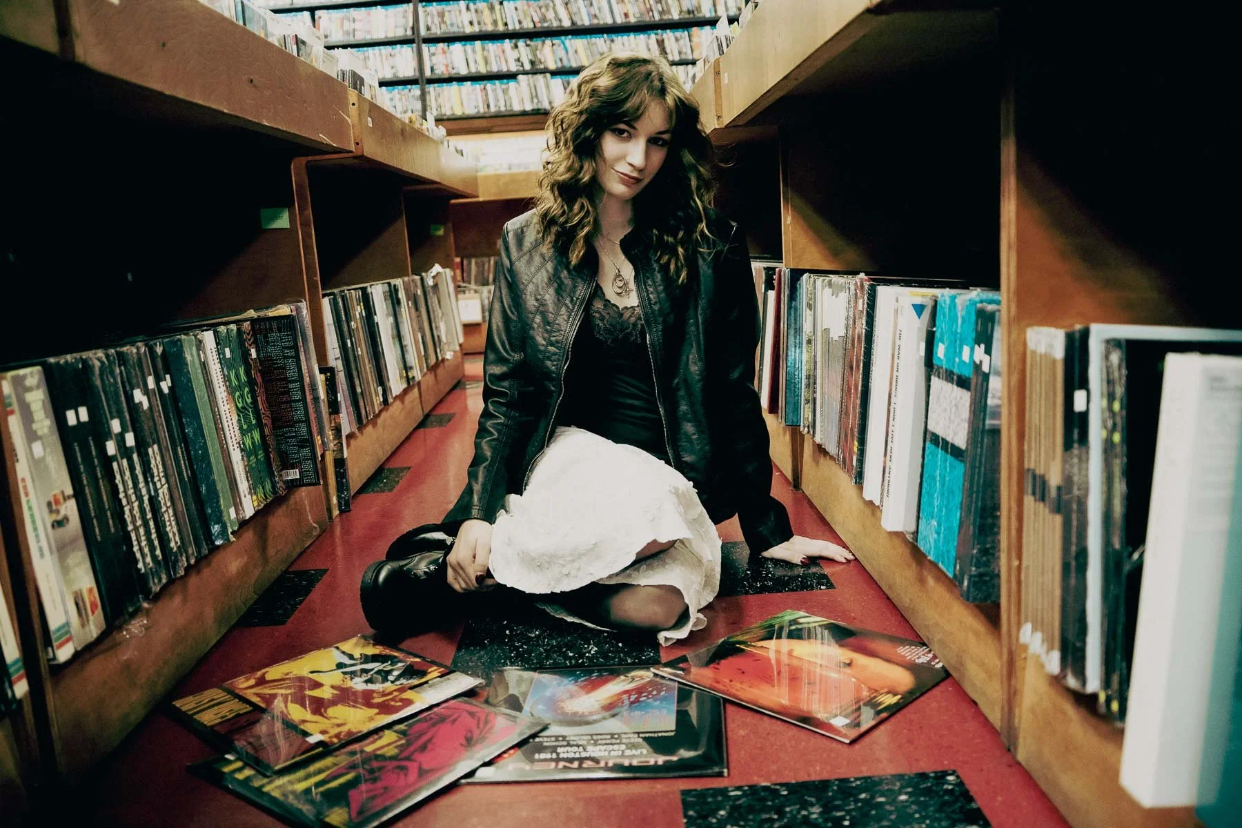 A girl posing on the floor in the aisles of a record shop
