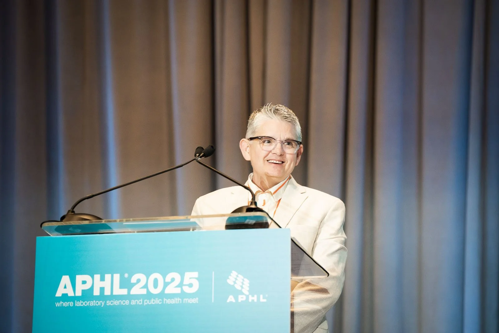 A smiling woman on stage at the APHL 2025 annual conference