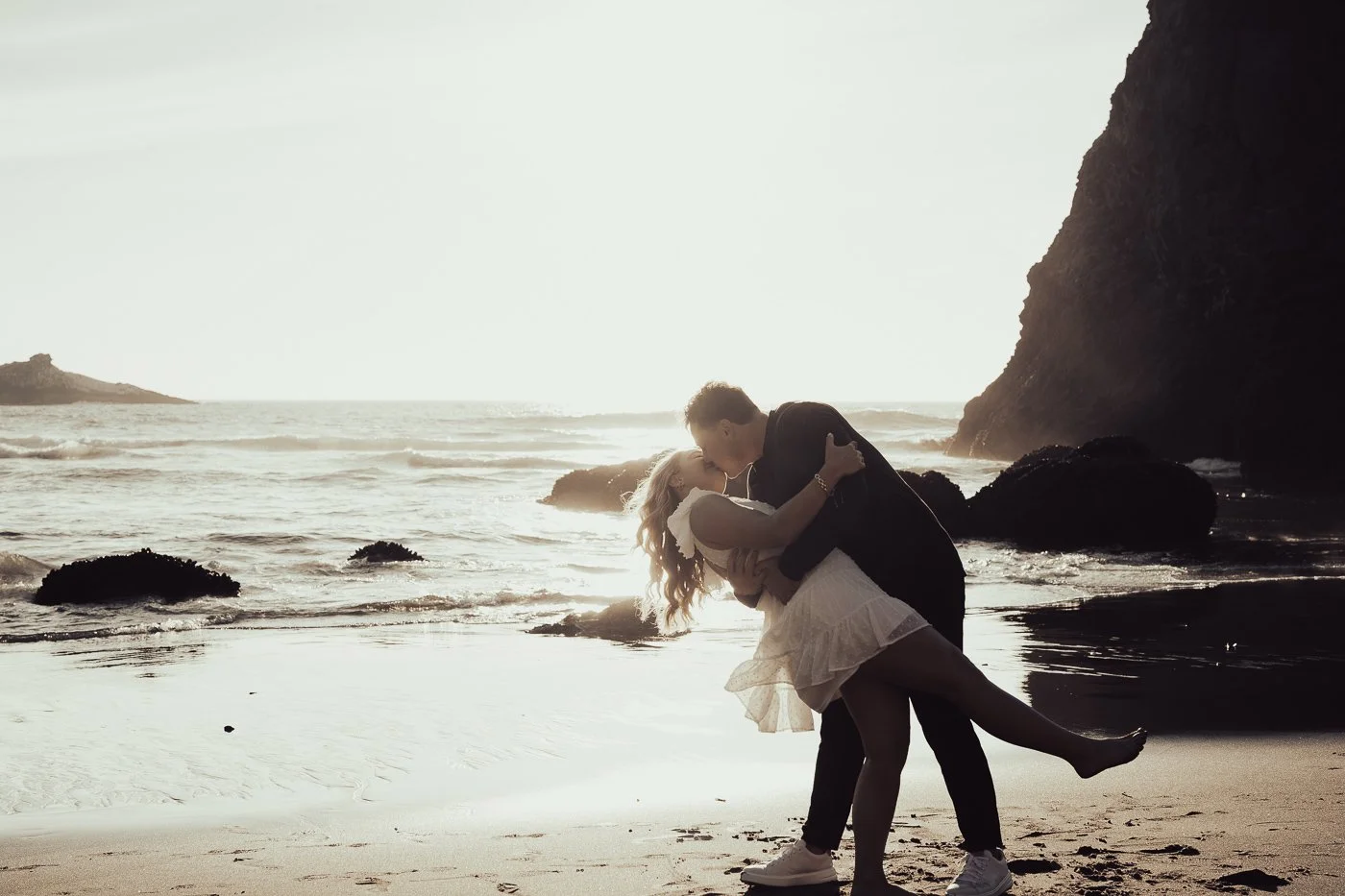 A couple dancing on the beach with large rock formations behind them