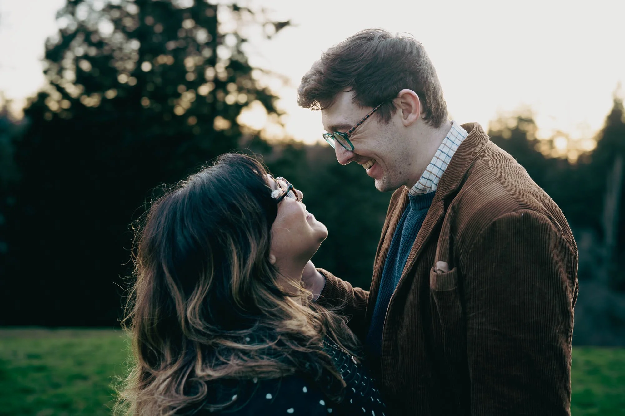 A laughing couple looks into each others eyes on a hill at Hoyt Arboretum