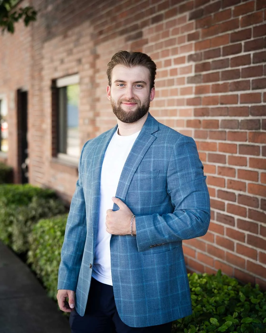 Casual business portrait of a man in a blue suit, set against a red brick wall