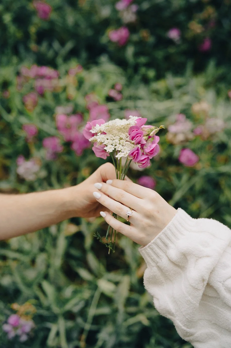 A couples hands holding a small bouquet of wild flowers